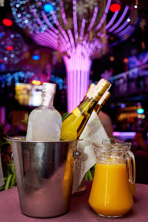 Bottle of cold vodka and wine bottle in bucket with ice and orange juice in jug on table, copy space.の写真素材
