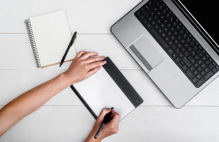 Top view of woman hands with graphic tablet drawing and retouching image on laptop computer, using...