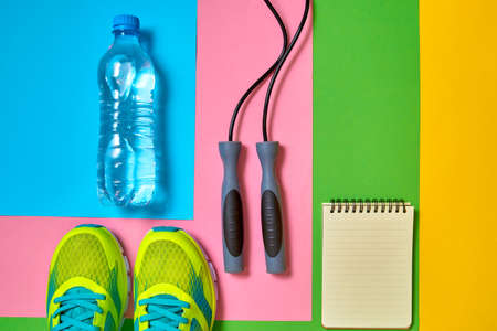 Top view of sport shoes, skipping rope, empty blank notebook and bottle of water on colorful background, copy space.の写真素材