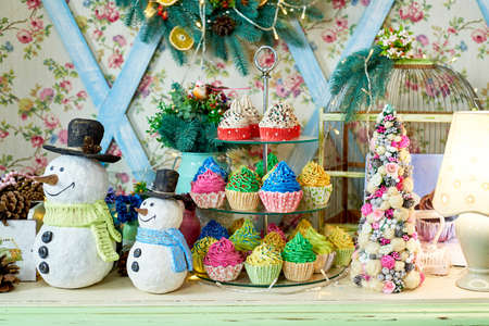 Christmas background with snowman, decorated Christmas tree and colorful cupcakes on wooden table, copy space. Festive snowmen with Christmas decorationsの写真素材