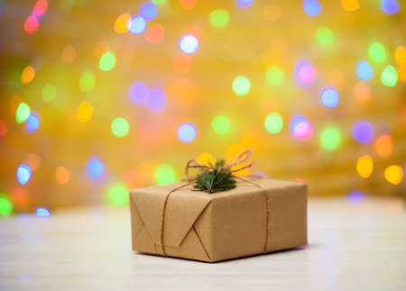 Christmas background with one gift box wrapped in kraft paper with fir tree branch on golden blured, sparkling background, copy space. Holiday greeting cardの写真素材