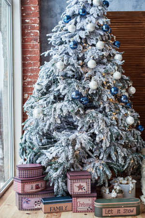 Christmas background with big Christmas fir tree with snow and white and blue decorations near window at home indoors, copy space. Winter holidays, family concept. Christmas morningの写真素材