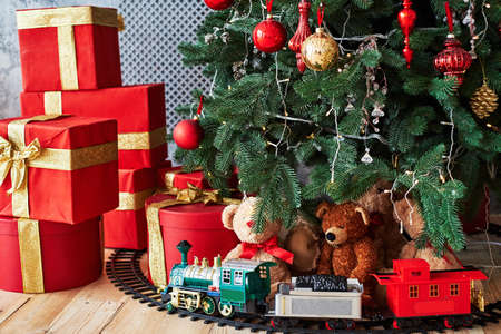 Christmas background with red gift boxes decorated with golden ribbon on floor and child toys under Christmas tree, copy space. Winter holidays conceptの写真素材