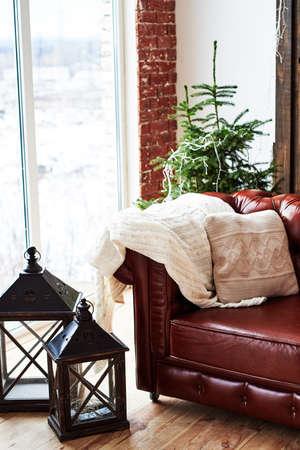Christmas interior with vintage brown leather sofa, fir tree and lanterns in loft room with panoramic window, copy spaceの写真素材