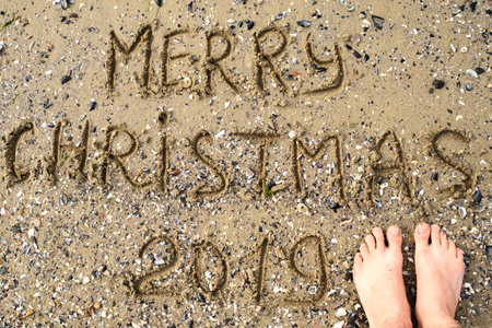 Merry Christmas 2019 written on tropical beach sand with man feet, copy space. Holiday concept, top...