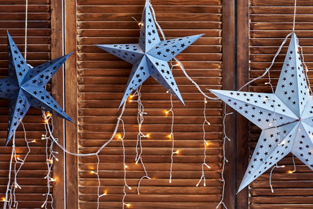 Decorative stars with lights on brown wooden wall, copy space. Christmas background with stars and garlandの写真素材