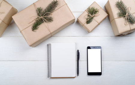 Christmas background with red gift boxes, mobile phone with white screen and blank notebook, copy space. Template for new year goal or resolutions. Christmas mockup. Flat lay, top viewの写真素材