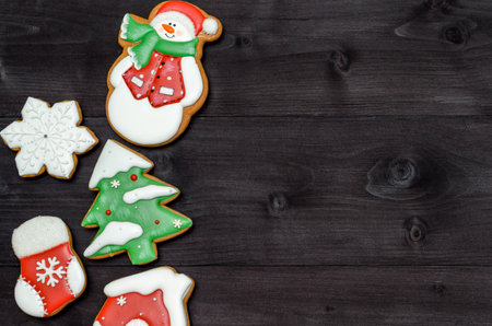 Tasty homemade gingerbread cookies with icing on dark wooden table, top view, flat lay. Christmas background with boder of snowman, snowflake, stocking, fir tree and house, copy space. Holiday foodの写真素材