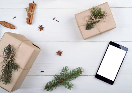 Mobile smart phone with blank white screen for app presentation with Christmas decorations, copy space. Christmas gifts on wooden background. Flat lay, top view. Application mock up templateの写真素材