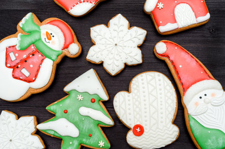 Tasty homemade gingerbread cookies with icing on dark wooden table, top view, flat lay. Christmas background with santa, snowman, snowflake, stocking, fir tree, mitten and house, copy spaceの写真素材
