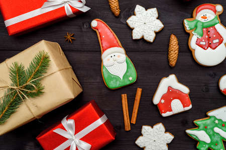 Christmas gingerbread cookies, gift boxes, cinnamon, cones, fir tree branches on dark wooden background, copy space. Top view, flat lay. Santa, snowflake, fir tree, house, snowman. Holiday conceptの写真素材