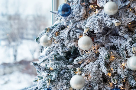 Closeup of Christmas tree decorated with white baubles and garland near window, copy space. Christmas decorations. Holiday background. Christmas tree. Greeting cardの写真素材