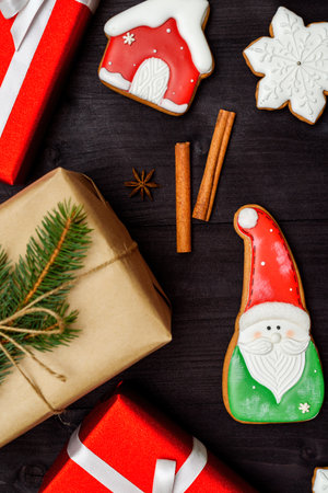 Christmas gingerbread cookies, gift box wrapped in craft paper with fir tree branch and cinnamon on dark wooden background, copy space. Top view, flat layの写真素材