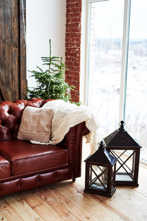 Christmas interior with vintage brown leather sofa, fir tree and lanterns in loft room with panoramic window, copy spaceの写真素材