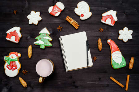 Homemade gingerbread cookies, cup of cocoa and open blank notebook on dark wooden table. Top view, flat lay. Christmas background with santa, snowman, snowflake, stocking, fir tree, copy spaceの写真素材