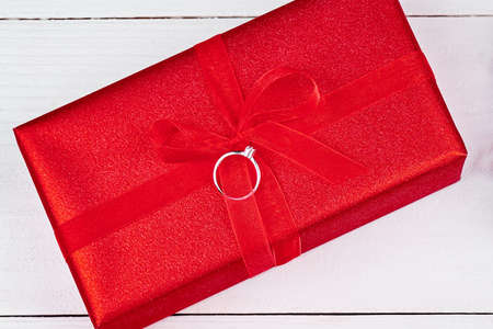 Red gift box with ribbon bow on white wooden background, copy space. Holiday greeting card. Mothers...