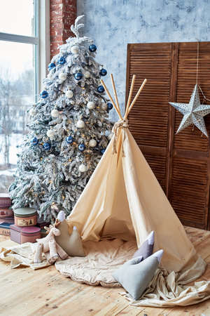 Christmas tree with gifts and wigwam near window in child room, copy space. Childen room interior with decorated play tipi tent. Scandinavian styleの写真素材