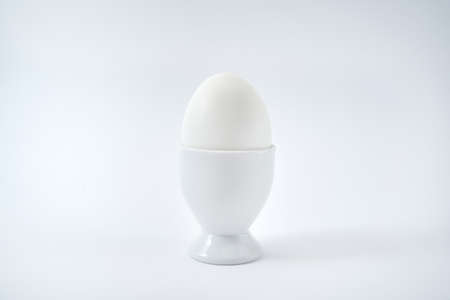 White egg standing on egg cup isolated on white background, copy space. Boiled egg in stand. Healthy food concept, minimalismの写真素材