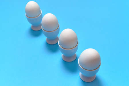 White eggs standing on egg cup isolated on blue background, copy space. Row of boiled eggs in stand....
