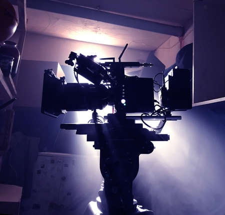 Mystical silhouette of a movie camera in the suns rays of light from the window. Camera on a tripod in standby modeの写真素材