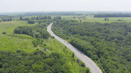 two cars drive each other along the road that is surrounded by forests, lakes, fields and meadows....