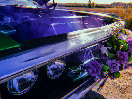 green retro car. a wedding retro car, decorated with flowers on a radiator grill, stands in the middle of a field with an open hood and blue smoke coming from the engine. broken carの写真素材