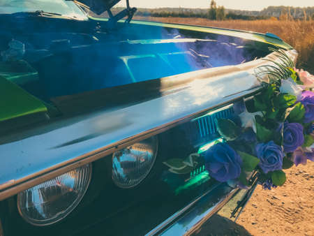 green retro car. a wedding retro car, decorated with flowers on a radiator grill, stands in the middle of a field with an open hood and blue smoke coming from the engine. broken carの写真素材