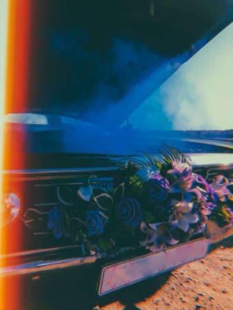 green retro car. a wedding retro car, decorated with flowers on a radiator grill, stands in the middle of a field with an open hood and blue smoke coming from the engine. broken carの写真素材