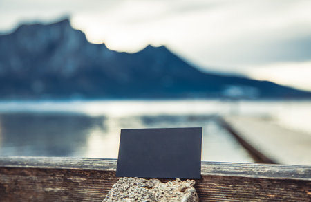 blank business card for your text and logo on the background of the Austrian mountain lake. black blank business card. black sheet of cardboard in hand and free standingの写真素材