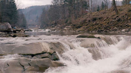 Waterfall in the Winter. Rapid Flow of Water from a Mountain Creek and Stone Rapids with Snow. The river Prut in Ukrainian Carpathians in Yaremche city.Melting ice and snow on the river in the forest.の写真素材