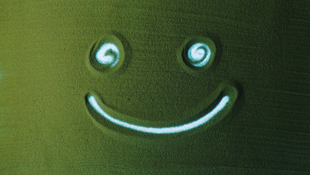 Hand drawing the Smile symbol in the Green Sand. Male hand writes peace symbol on the green sand with white backlight. Top view 4k resolutionの写真素材
