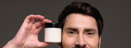 Banner crop of adult man holding cosmetic cream isolated on gray background