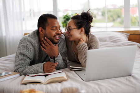Smiling asian woman in eyeglasses hugging african american boyfriend during online education near...