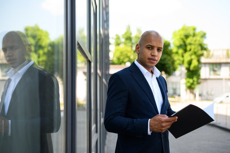 African american businessman holding documents and looking at camera near buildingの写真素材