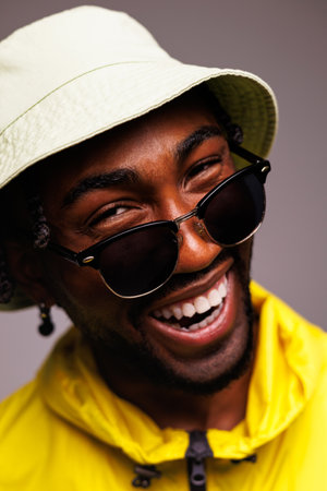 Portrait of cheerful African American man in sunglasses and stylish streetwear looking at camera isolated on grayの写真素材