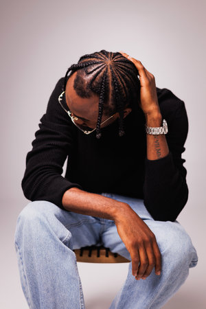 Stylish young african american man with braids wearing eyeglasses, turtleneck and jeans while...