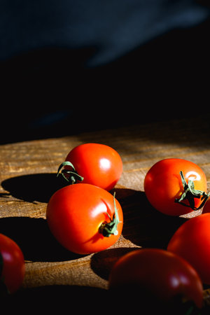 Cherry tomatoes on wooden table with sunlight on black background