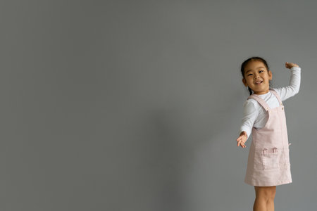 Cheerful Korean baby girl in sundress looking at camera on gray background