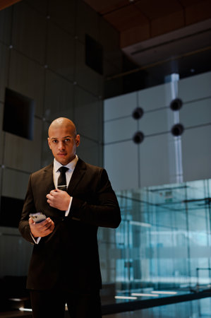 African american businessman in suit holding cellphone in hall of officeの写真素材