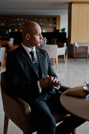 African american businessman in classic attire sitting near smartphone in cafe of business center