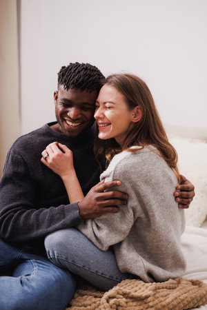 Cheerful multiethnic couple cuddling while sitting on bed at home