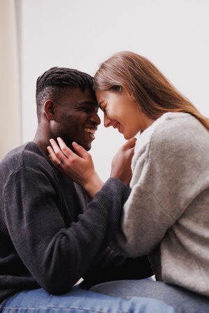 Smiling diverse couple in casual clothes and jeans hugging at home
