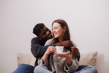 Smiling african american man hugging girlfriend with coffee in bedroom at home