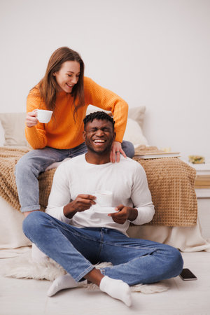 Smiling multiethnic couple having fun during morning coffee in bedroom