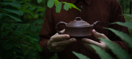 Man holding Chinese clay tea pot near leaves in summer forest