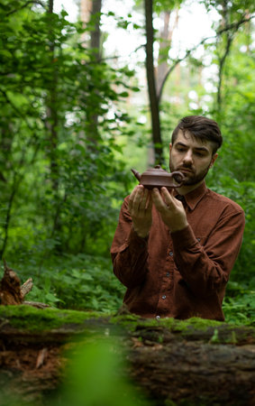 Young man holding Chinese teapot in summer forestの写真素材