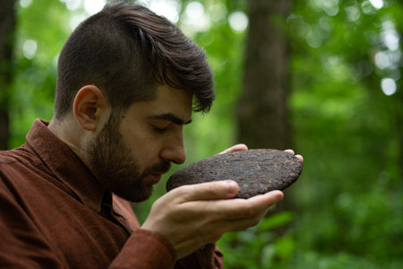 Bearded man smelling pressed disk of shu pu-erh tea in forest