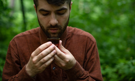 Bearded man holding tea bowl of shu puer in summer forest