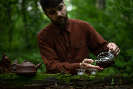 Man pouring shu puer tea in cha hai on log in moss in forest