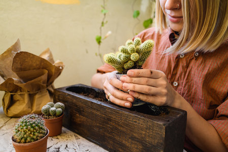 Young woman with dirty hands planting cactus near soil and flowerpot on tableの写真素材